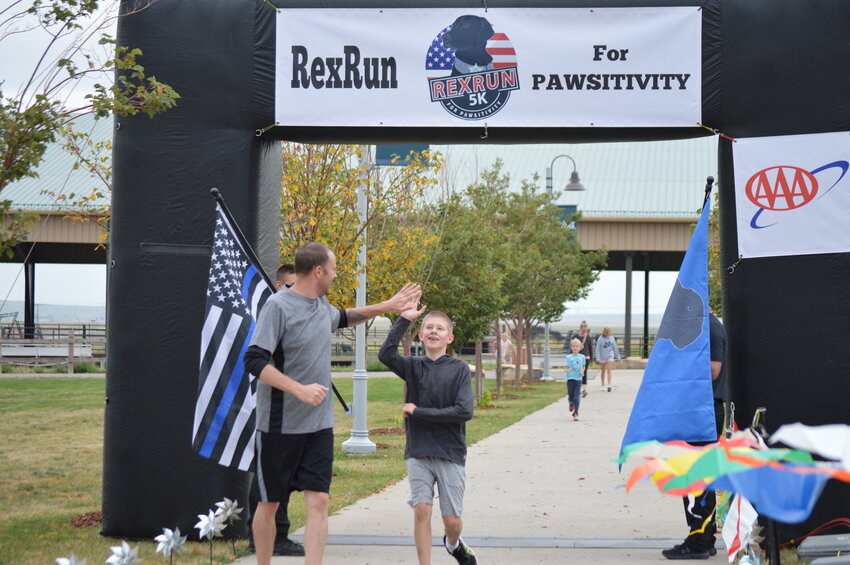 A large smile spread across 11-year-old Clay McCollum’s face as he gave a high-five to his dad, Luke McCollum, after crossing the 1-mile finish line at the second annual RexRun for PAWSitivity event on Aug. 26.
